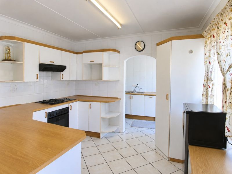 Functional kitchen featuring white cabinetry, laminate countertops, gas hob, and built-in oven, with an adjoining scullery area accessible through an arched doorway.