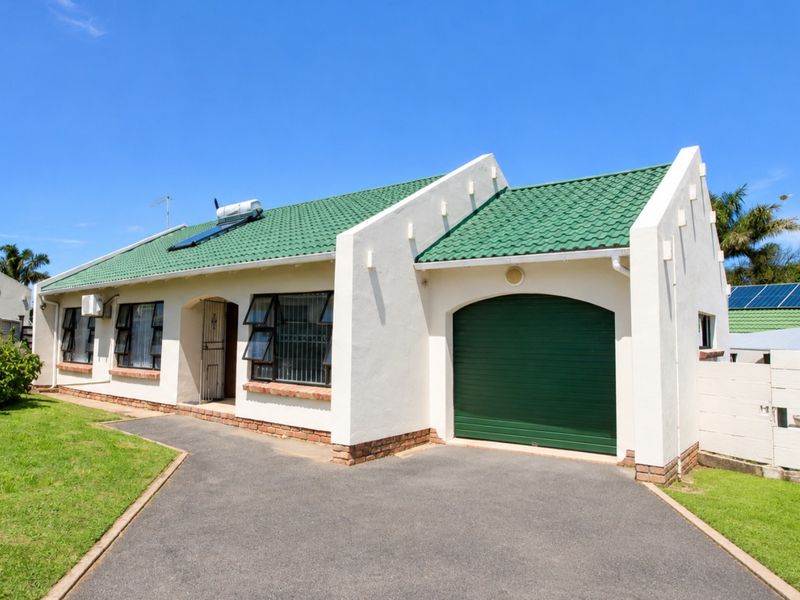 Front elevation of a townhouse featuring a green tiled roof, solar water heater, integrated garage, and paved driveway with surrounding lawn.