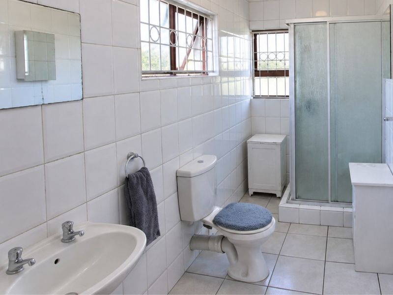 A functional bathroom featuring a shower enclosure, pedestal basin, and toilet, finished with full-height wall tiling and tiled flooring.