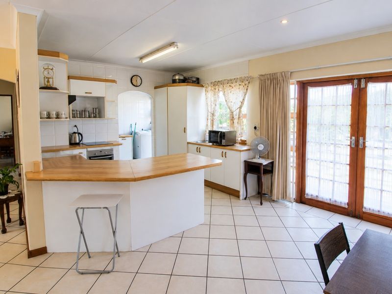 A functional kitchen featuring built-in cabinetry, laminate countertops, and tiled flooring, with direct access to the outdoor area through wooden french doors.