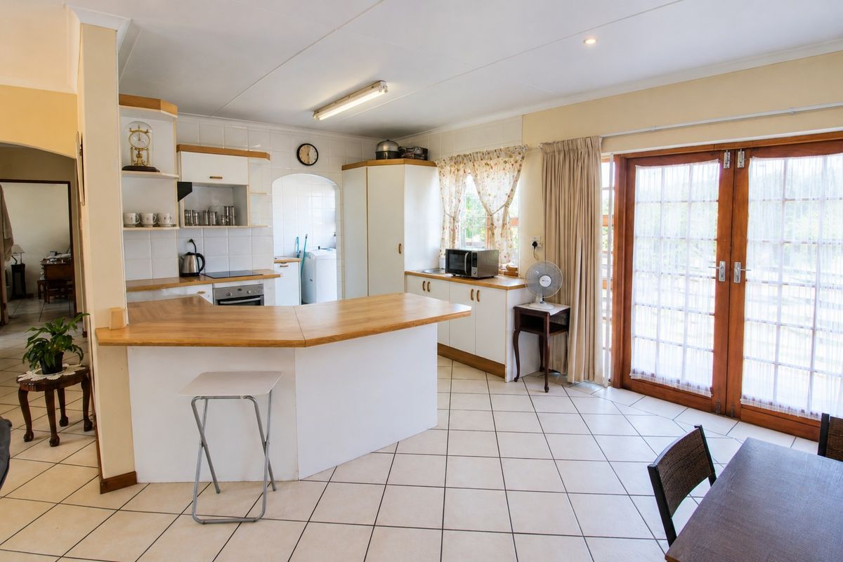 A functional kitchen featuring built-in cabinetry, laminate countertops, and tiled flooring, with direct access to the outdoor area through wooden french doors.
