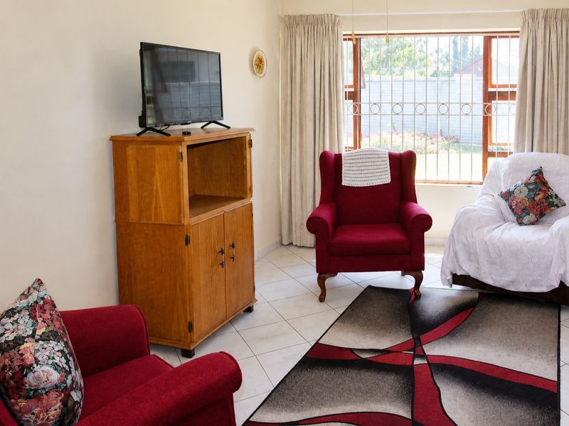 A comfortable living room featuring tiled flooring and a large window fitted with security bars, offering a view of the garden.