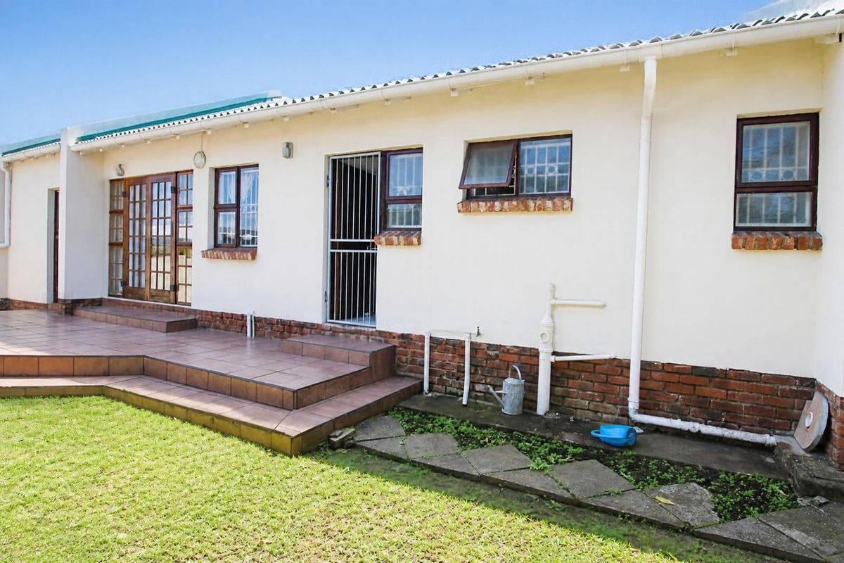 Rear exterior view of the townhouse featuring a tiled patio, brick base detailing, and multiple access points with security gates and windows.