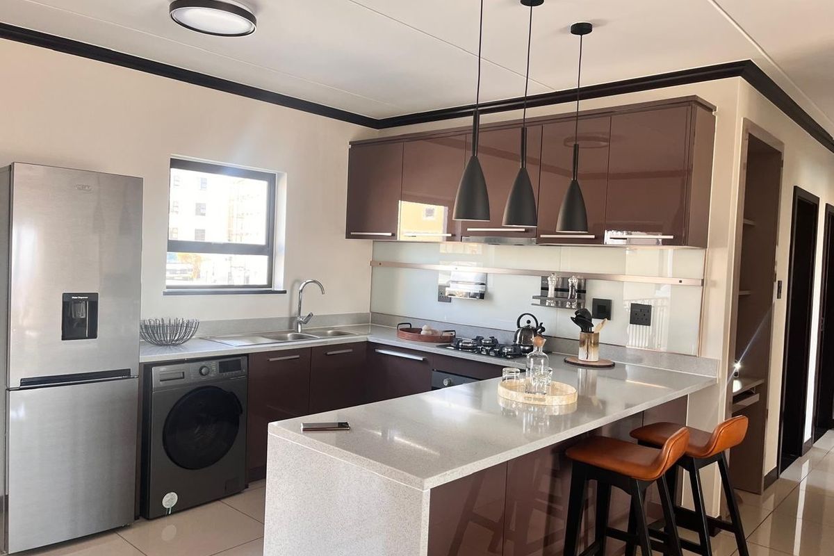 Modern kitchen featuring high-gloss cabinetry, stone countertops, a breakfast bar, and integrated lighting, offering a sleek and functional culinary space.