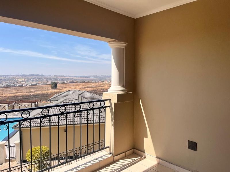 A covered balcony featuring a decorative column, wrought iron balustrade, and tiled flooring, offering expansive views over the surrounding estate.