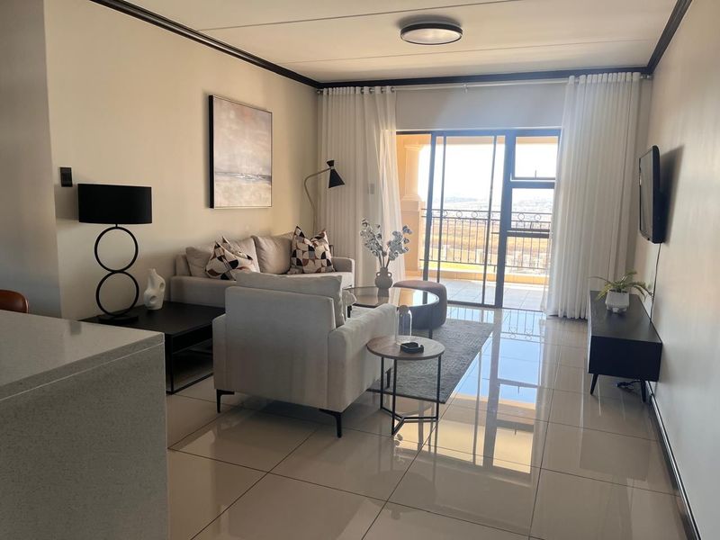 A bright and modern living room featuring large format floor tiles, crown molding, and a sliding glass door leading to a balcony.