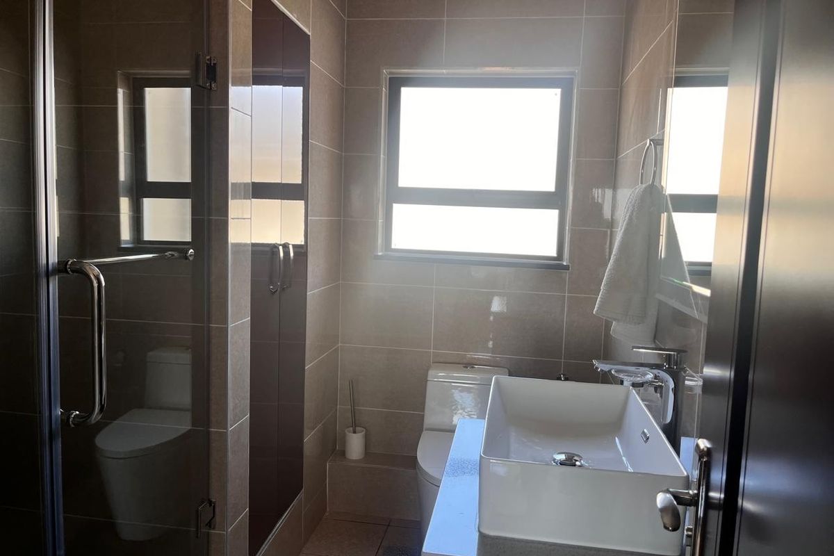 Modern bathroom featuring a vessel sink on a stone vanity, a glass-enclosed shower, and neutral ceramic tiling throughout.