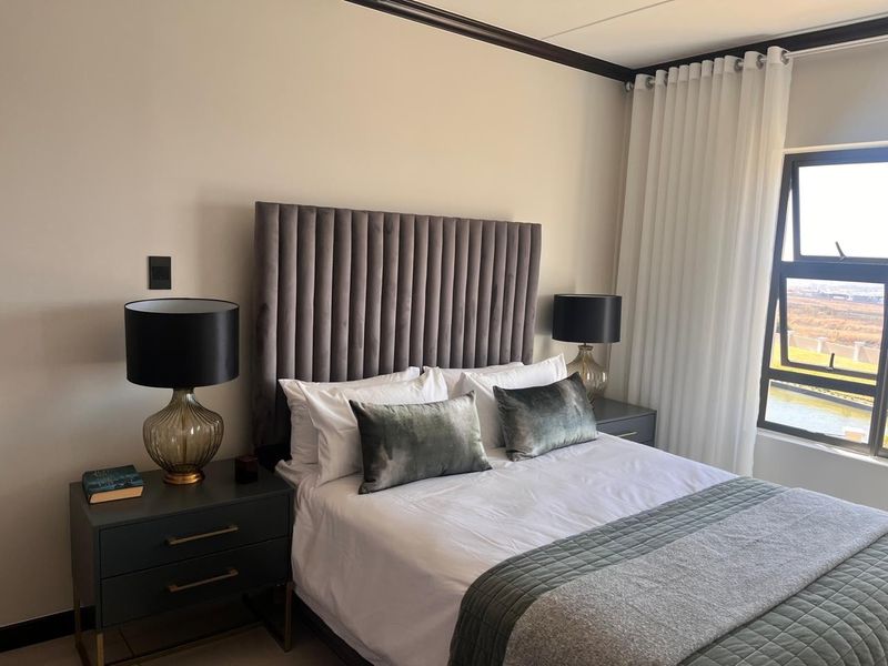 A well-maintained bedroom featuring neutral walls, crown molding, and a large window with natural light and views.