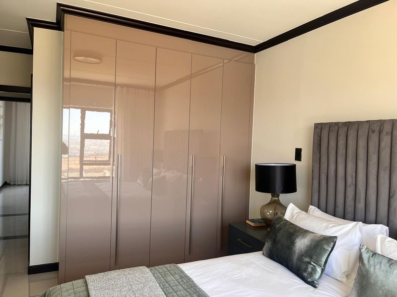 A well-maintained bedroom featuring modern high-gloss built-in cupboards, crown molding, and tiled flooring.