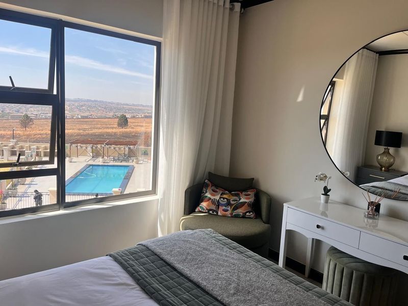 A well-lit bedroom featuring a large window with views overlooking the complex pool area and surrounding landscape.