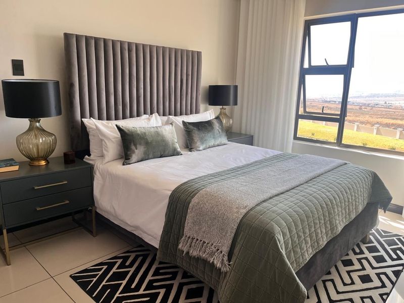 A well-maintained bedroom featuring tiled flooring, a large window with natural light, and neutral wall finishes.