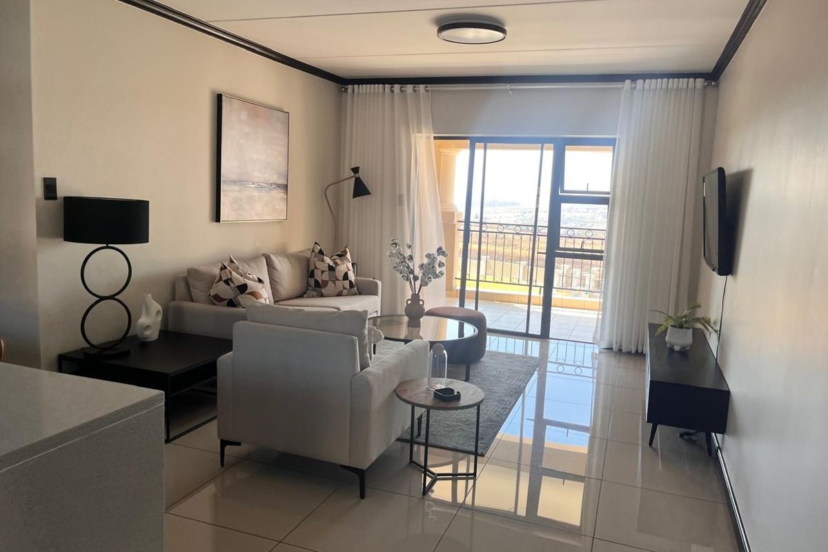 A bright and modern living room featuring large format floor tiles, crown molding, and a sliding glass door leading to a private balcony.