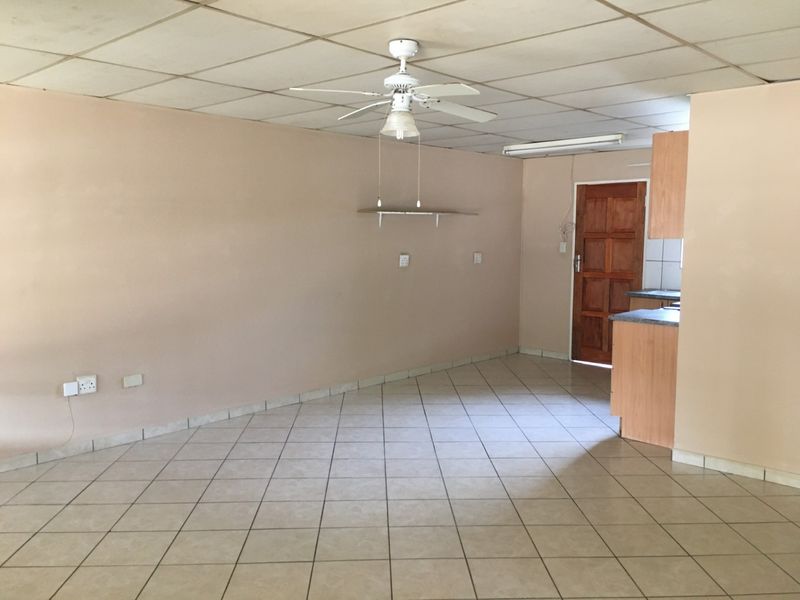 An open-plan living and kitchen area featuring tiled flooring, a ceiling fan, and drop ceiling tiles, offering a blank canvas for renovation.