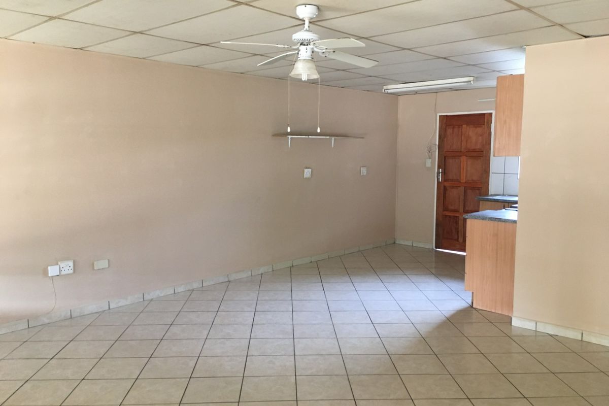 An open-plan living and kitchen area featuring tiled flooring, a ceiling fan, and drop ceiling tiles, offering a blank canvas for renovation.