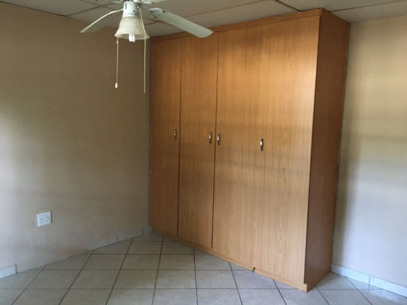A bedroom featuring built-in wooden wardrobes, tiled flooring, and a ceiling fan, offering a functional and neutral space.