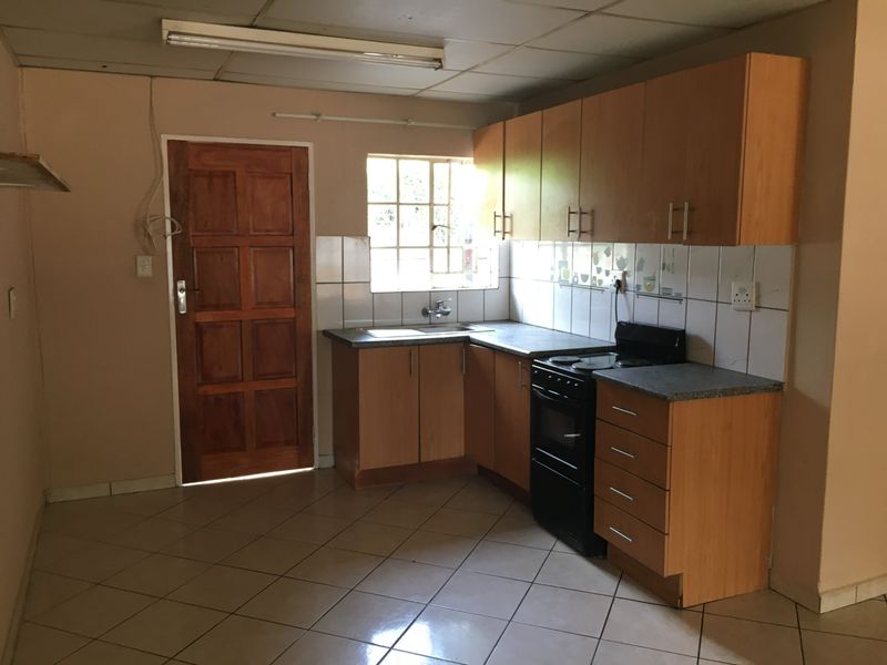 A functional kitchen featuring wooden cabinetry, laminate countertops, a tiled backsplash, and a freestanding stove, offering potential for modernization and cosmetic updates.