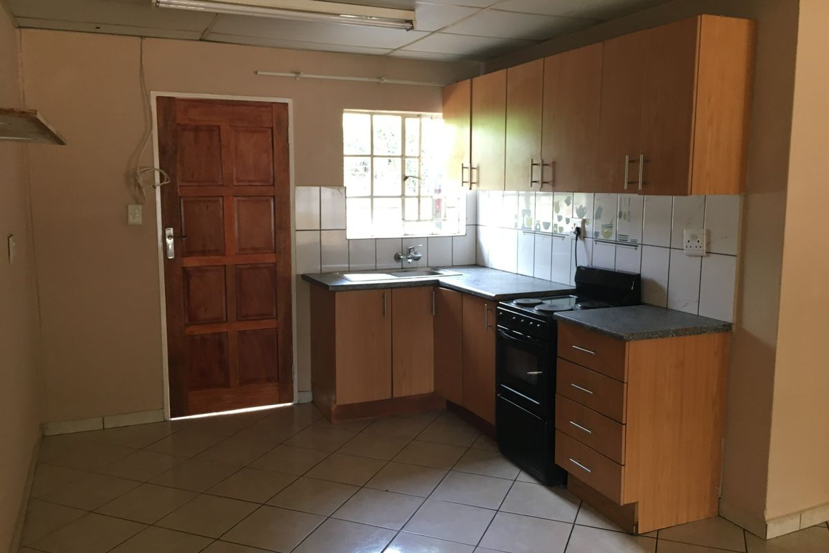 A functional kitchen featuring wooden cabinetry, laminate countertops, a tiled backsplash, and a freestanding stove, offering potential for modernization and cosmetic updates.