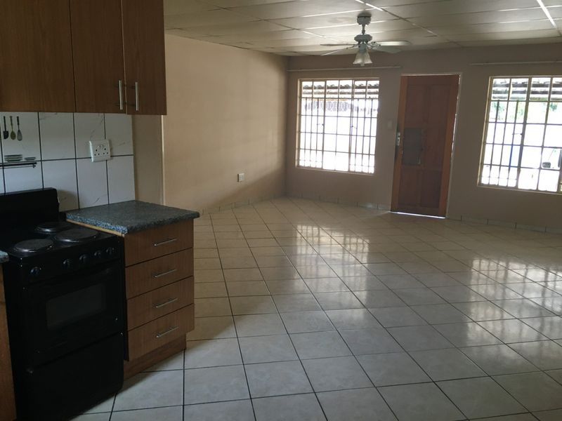 Open-plan living area featuring tiled flooring, a functional kitchen with built-in cabinetry, and large windows with security bars.