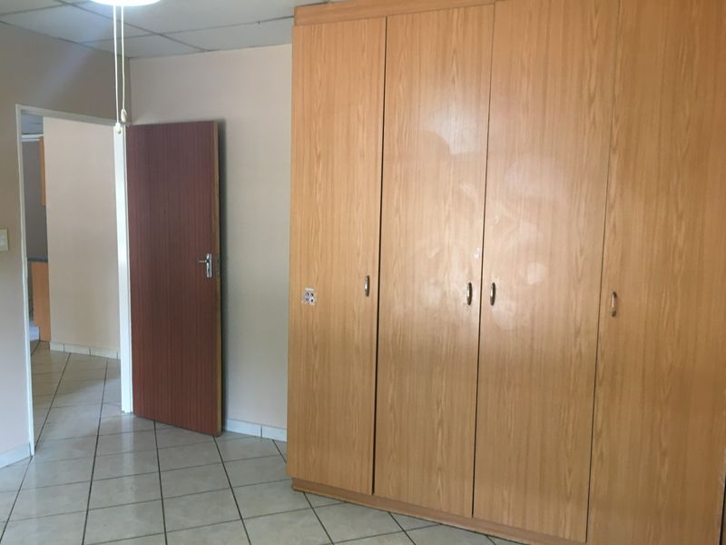 A bedroom featuring built-in wooden cupboards and tiled flooring, offering a clean and functional space.