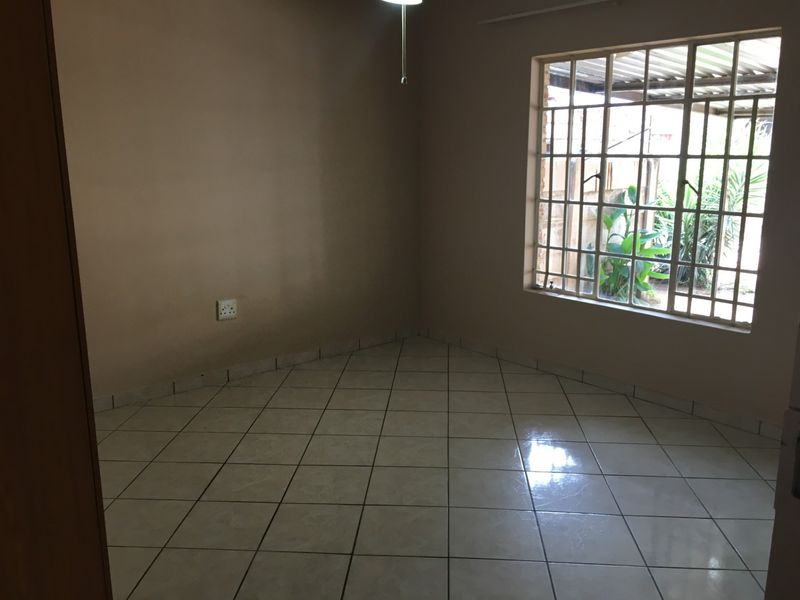 An empty bedroom featuring neutral wall paint, tiled flooring, and a window fitted with security bars.