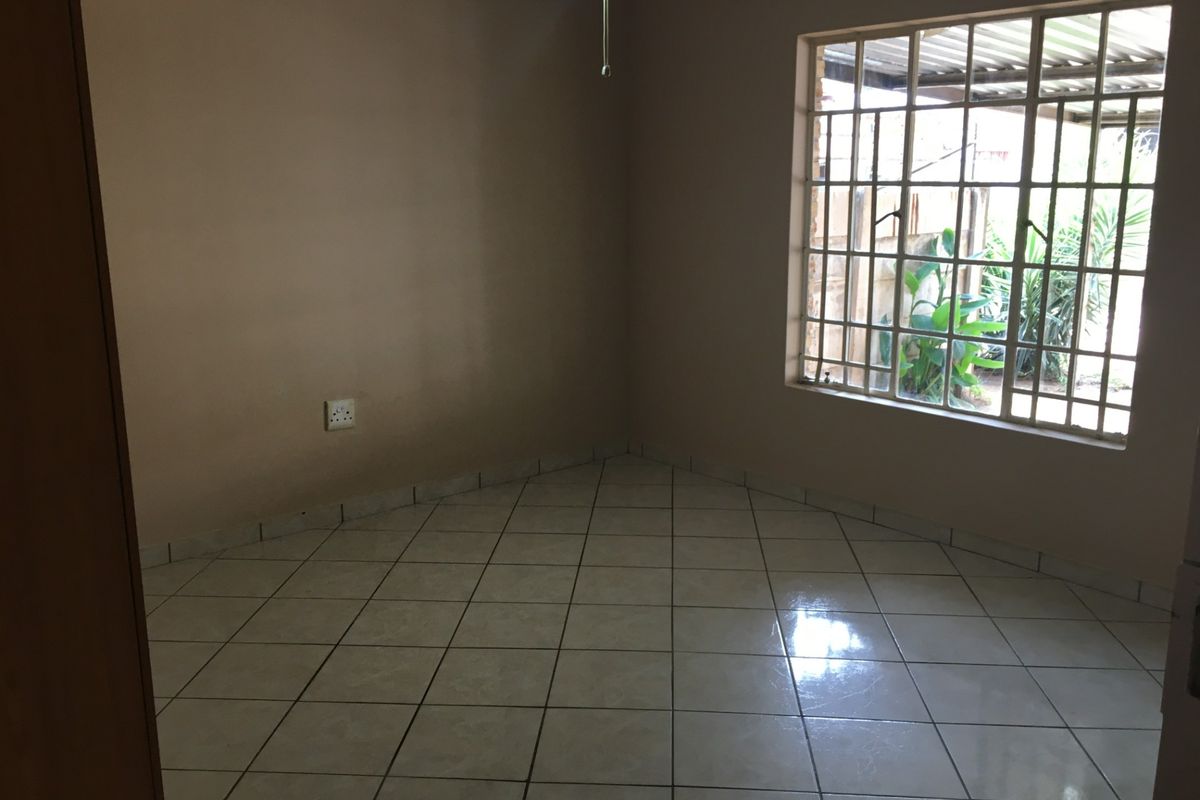 An empty bedroom featuring neutral wall paint, tiled flooring, and a window fitted with security bars.