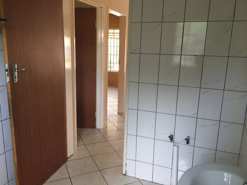 A view of a tiled hallway connecting multiple rooms, featuring dated wall tiles and standard internal doors in an empty apartment setting.