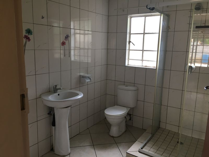 A functional bathroom featuring a pedestal basin, toilet, and a glass-enclosed shower with full-height wall tiling and tiled flooring.