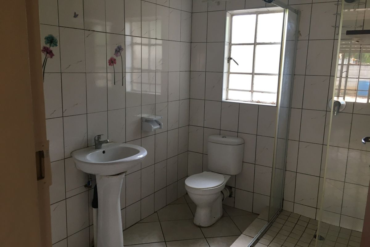 A functional bathroom featuring a pedestal basin, toilet, and a glass-enclosed shower with full-height wall tiling and tiled flooring.