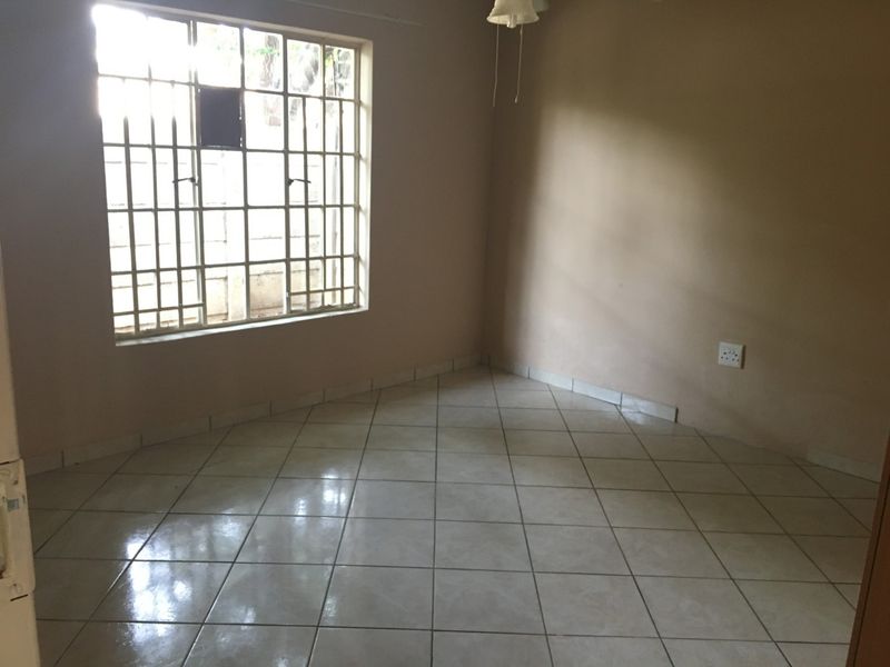 An empty bedroom featuring neutral tiled flooring, a window with security bars, and a simple ceiling light fixture.