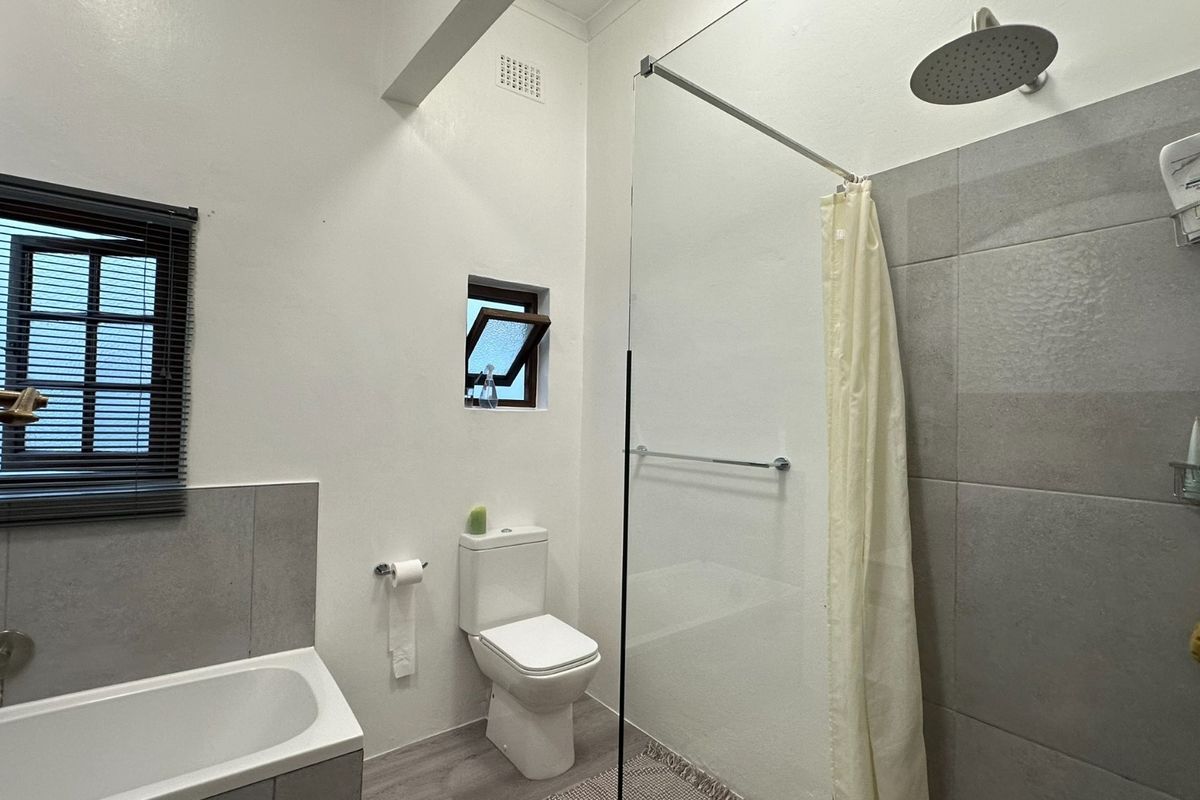 Modern bathroom featuring a built-in bathtub, a glass-enclosed shower with a rain shower head, and neutral grey tiling.