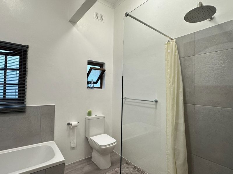Modern bathroom featuring a built-in bathtub, a glass-enclosed shower with a rain shower head, and neutral grey tiling.