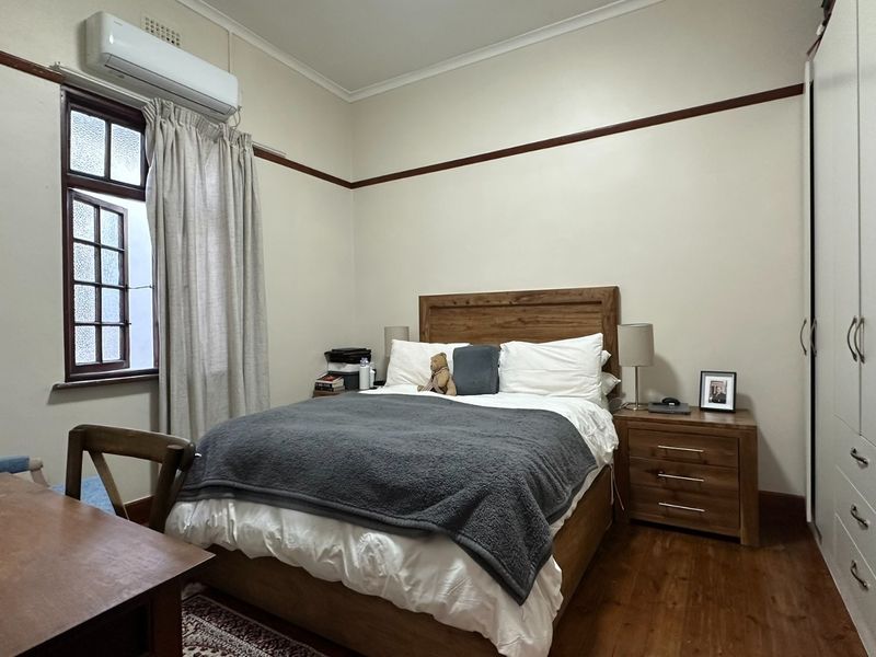 A well-maintained bedroom featuring timber flooring, a built-in wardrobe, and a wall-mounted split-system air conditioner.