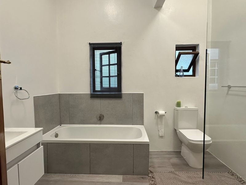 Modern bathroom featuring a built-in bathtub, glass-enclosed shower, vanity unit, and toilet with neutral grey tiling and clean white finishes.