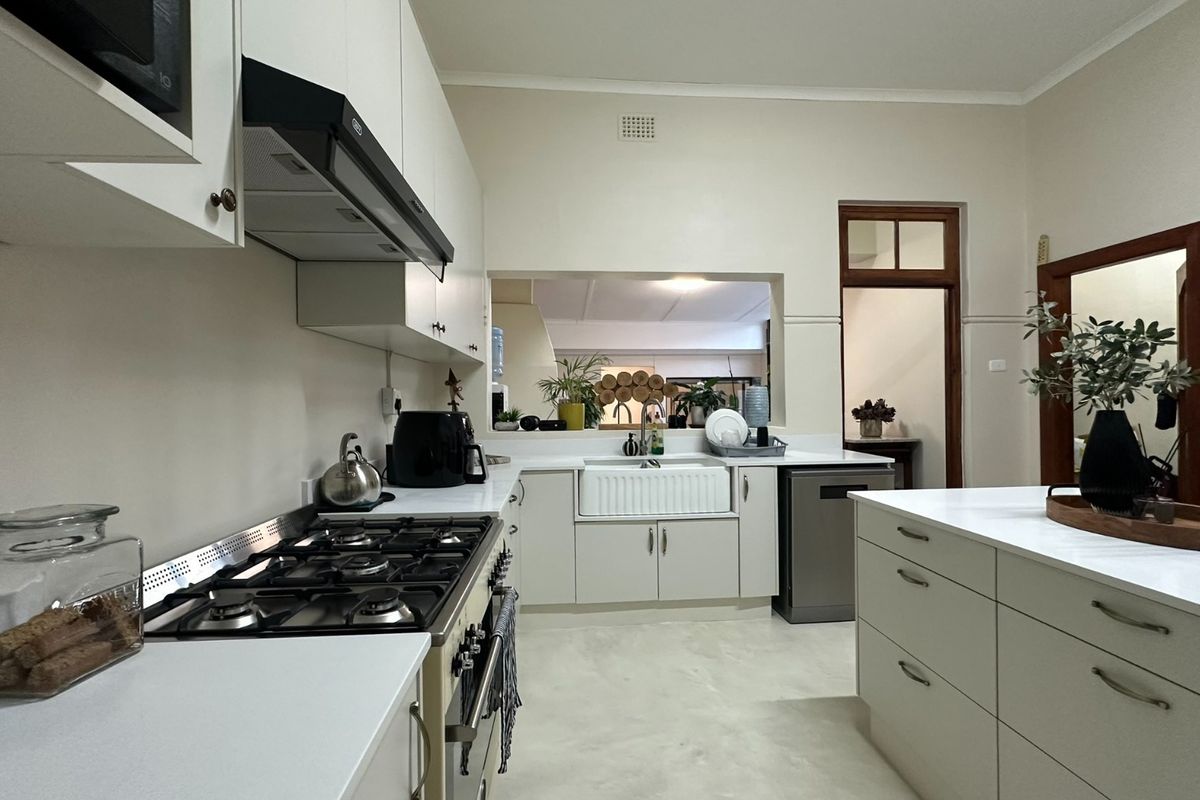 Modern kitchen featuring white cabinetry, stone countertops, a central island, gas hob, and a classic apron sink, offering a clean and functional workspace.