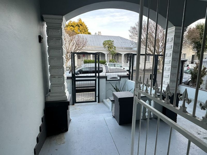 A covered front patio area featuring decorative columns, an arched entryway, and a secure metal gate leading to the street.
