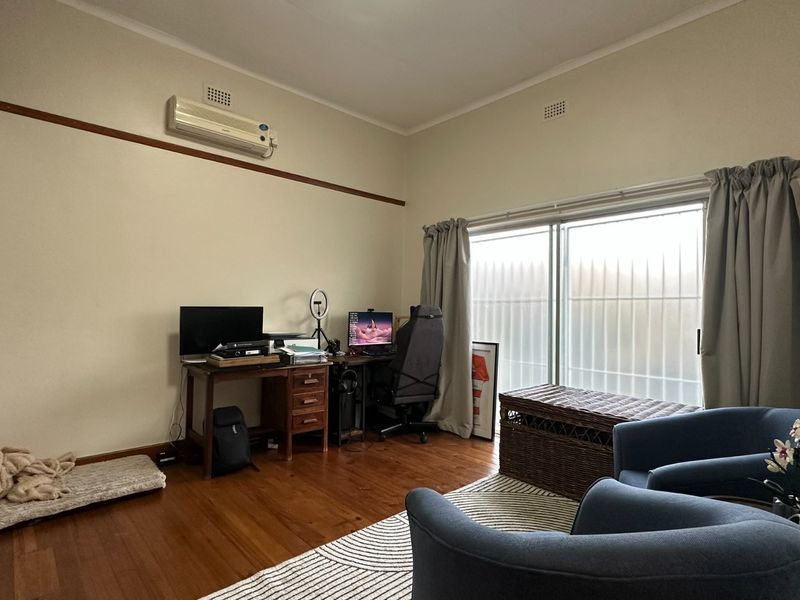 Bedroom featuring timber flooring, built-in cupboards, and a split-system air conditioner, with direct access to the outdoors via a sliding glass door.