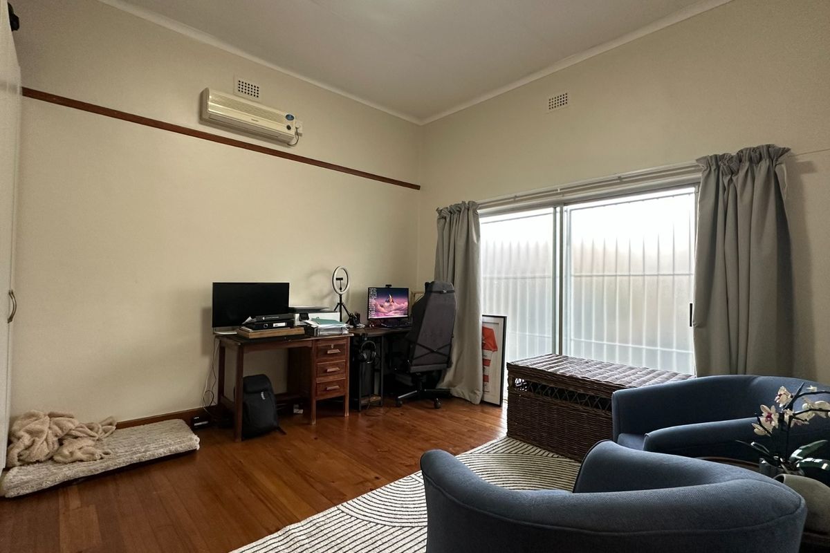 Bedroom featuring timber flooring, built-in cupboards, and a split-system air conditioner, with direct access to the outdoors via a sliding glass door.