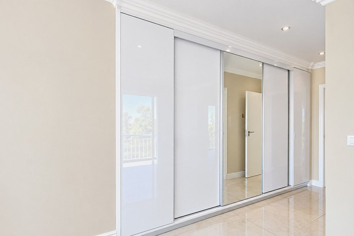 A bright bedroom featuring modern floor-to-ceiling built-in sliding wardrobes with a mirrored panel, recessed lighting, and polished tiled flooring.