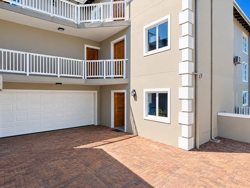 Front elevation of a modern townhouse featuring a paved driveway, integrated garage, and multi-level balconies with white railings.