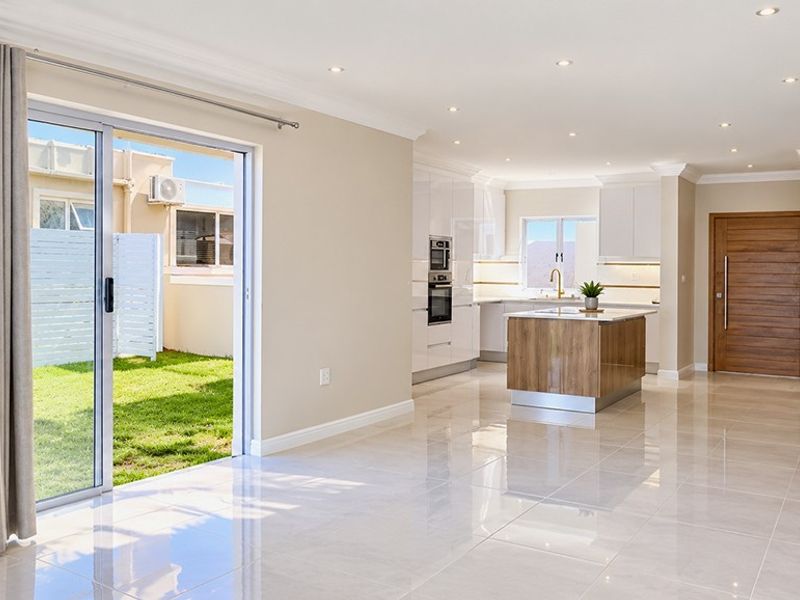 Modern open-plan living area featuring a sleek kitchen with built-in appliances, a central island, and seamless access to the rear garden through sliding doors.