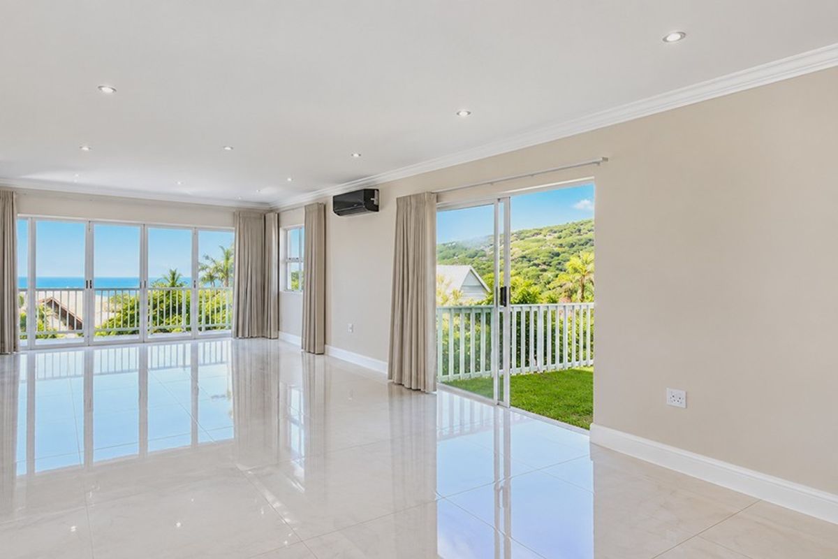 Spacious, light-filled living area featuring polished tile floors, recessed lighting, and large sliding glass doors opening to a balcony with scenic coastal views.