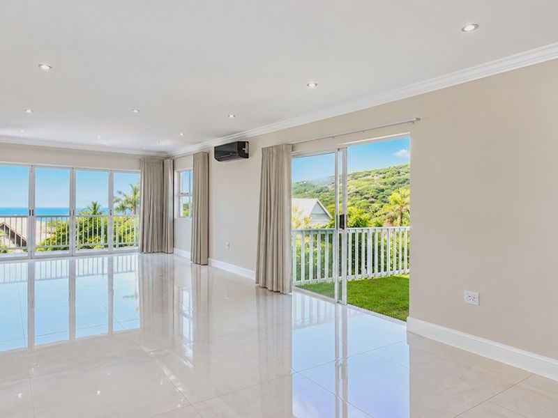 Spacious, light-filled living area featuring polished tile floors, recessed lighting, and large sliding glass doors opening to a balcony with scenic coastal views.