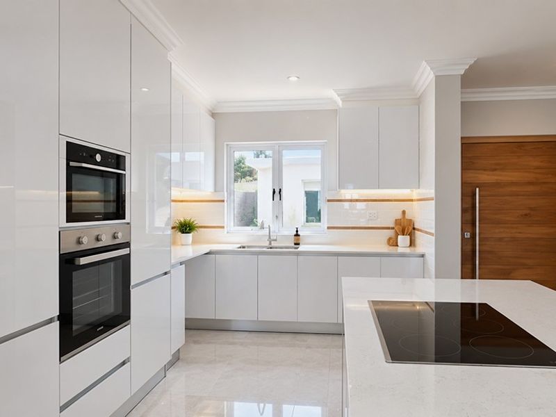Modern kitchen featuring high-gloss white cabinetry, stone countertops, a central island with an induction cooktop, and integrated built-in appliances.