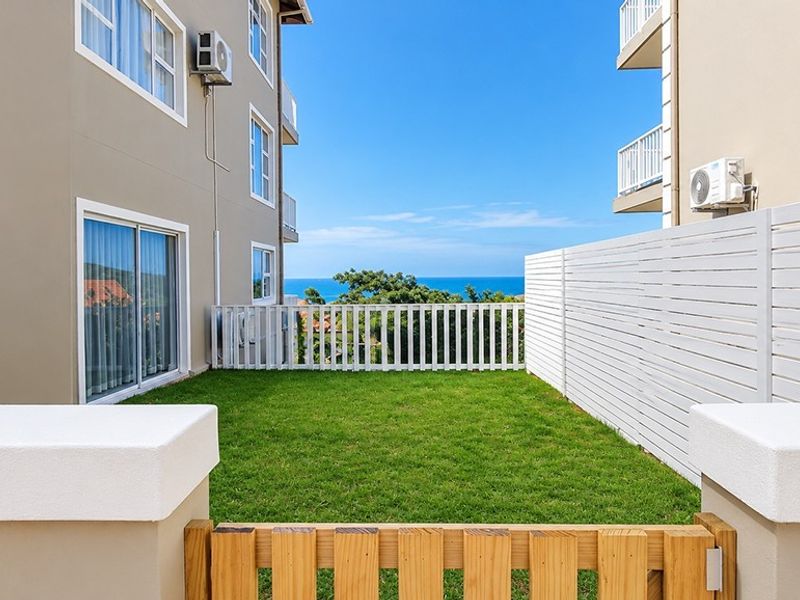 A well-maintained rear garden area featuring a lawn, white fencing, and sliding door access, offering a pleasant view towards the ocean.