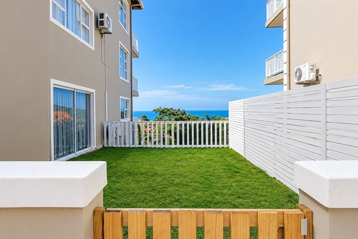 A well-maintained rear garden area featuring a lawn, white fencing, and sliding door access, offering a pleasant view towards the ocean.