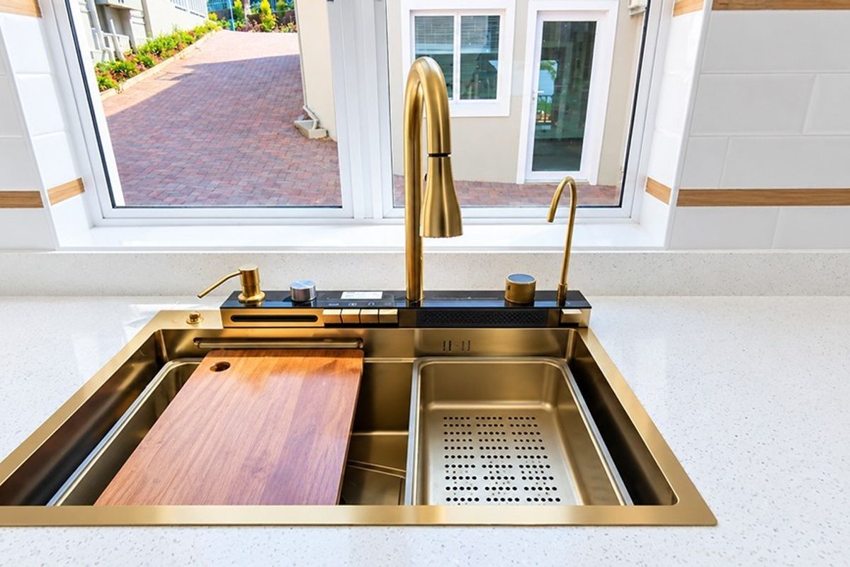 A modern kitchen sink area featuring a premium gold-tone workstation sink, gooseneck faucet, and clean quartz countertops with a subway tile backsplash.