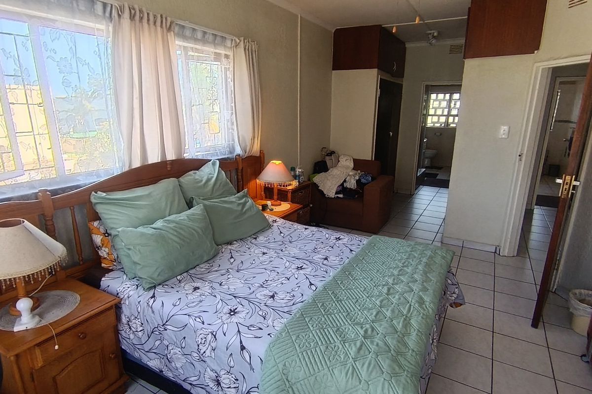 A bedroom featuring tiled flooring, built-in cupboards, and windows fitted with security bars, providing access to an adjacent bathroom area.