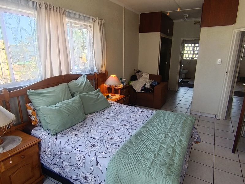 A bedroom featuring tiled flooring, built-in cupboards, and windows fitted with security bars, providing access to an adjacent bathroom area.