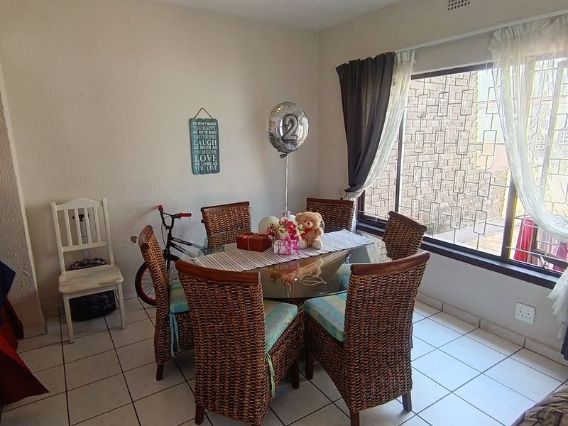 A bright dining area featuring tiled flooring and a large window with security burglar bars, providing natural light to the space.