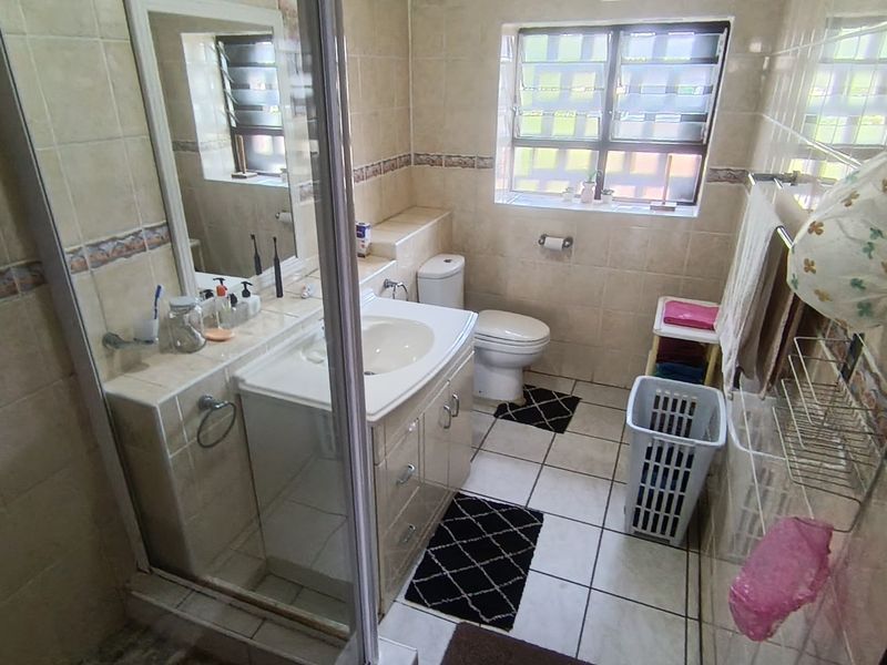A functional bathroom featuring a vanity cabinet with integrated basin, a toilet, and a glass-enclosed shower, finished with neutral wall and floor tiling.